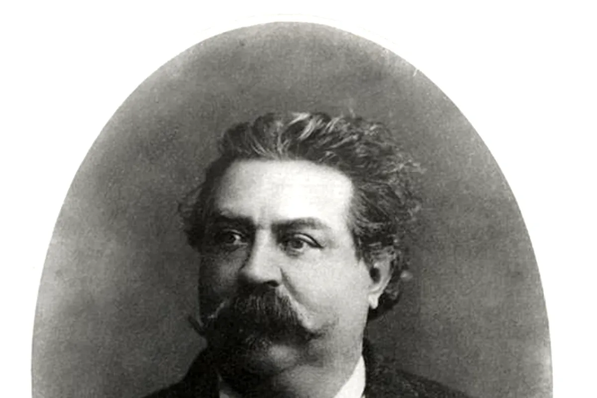 A black-and-white oval portrait of a man with thick curly hair, a large moustache and a dark jacket with a bow tie