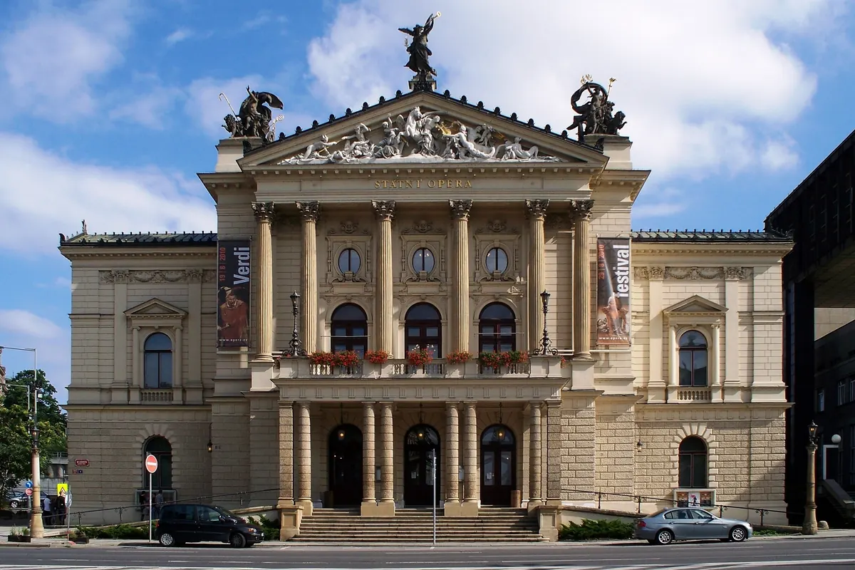 The cream-coloured neo-Renaissance facade of the State Opera in Prague, with a portico of columns, flower boxes and sculptures on the roof