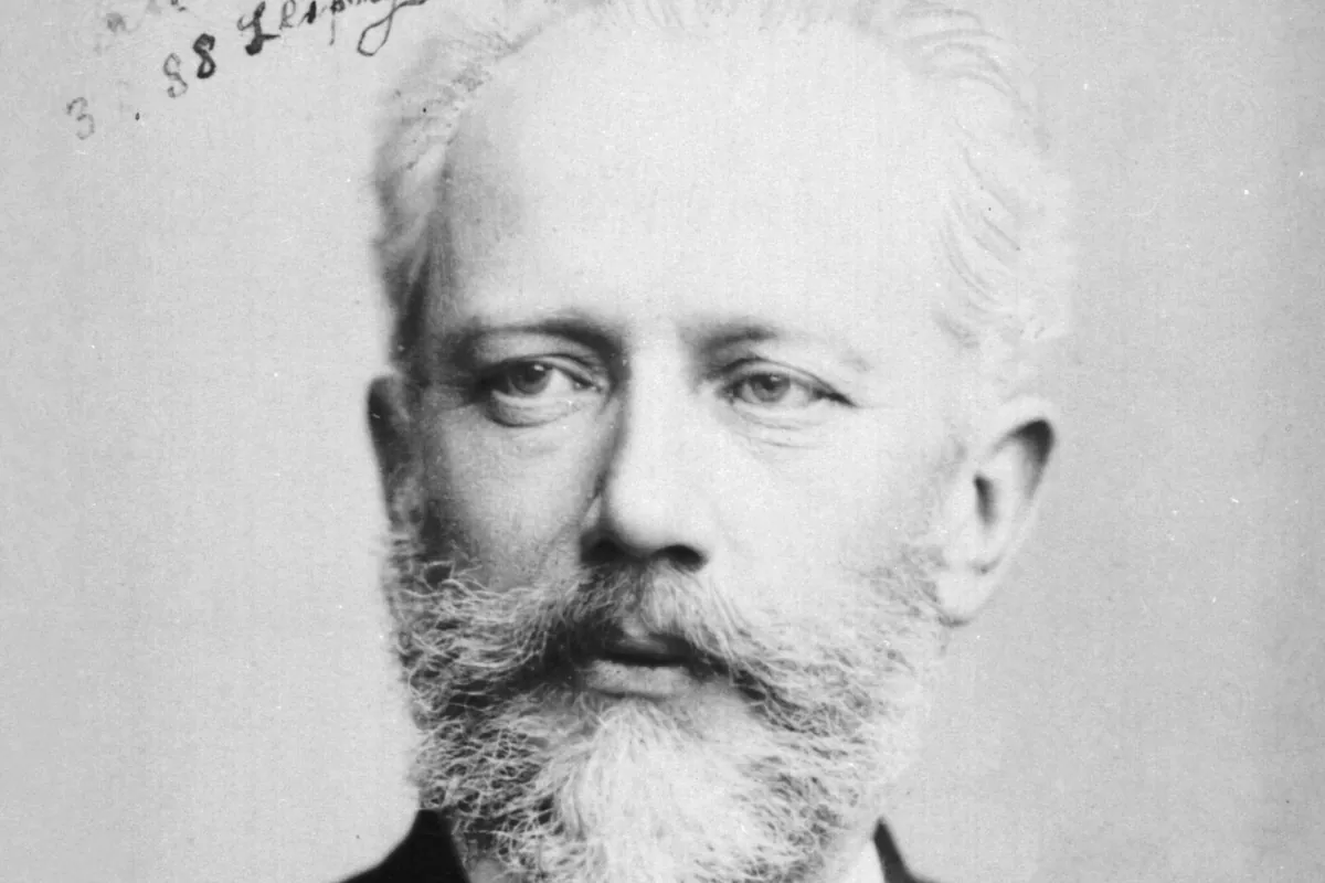 A black-and-white studio photograph of Pyotr Ilyich Tchaikovsky in 1888, a grey-bearded man with thinning hair looking at the camera, with handwriting at the top of the card