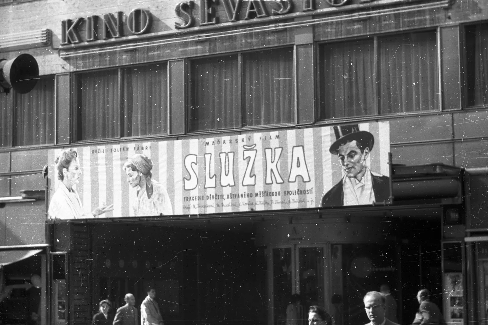A black-and-white photograph from 1958 of the Sevastopol cinema on Na Příkopě, the building that is now the Broadway, with a film poster above the entrance and people passing below